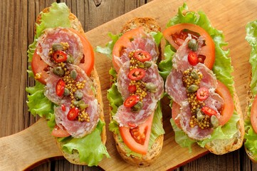 Sandwiches with ham, salad leaves, chili, tomatoes, capers, fren