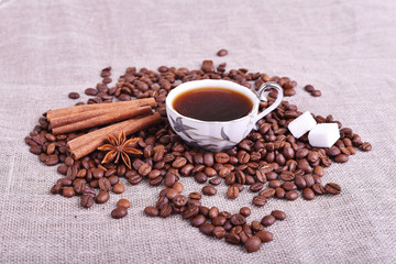 Cup of coffee with coffee beans, sugar, cinnamon on linen table