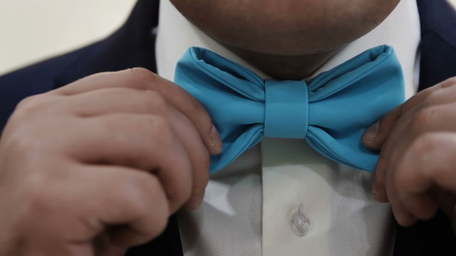 the man adjusts his blue bow tie close up