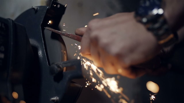 Close up the hands of a sharpening  axe on an electrical grinder