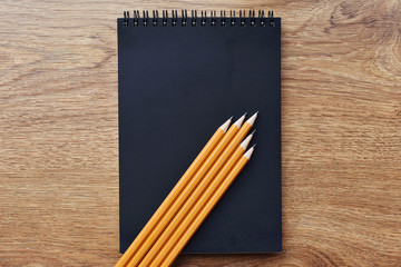 Black blank notebook on wood background with yellow pencils - Powered by Adobe