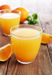 Glasses of orange juice with oranges on wooden table close up