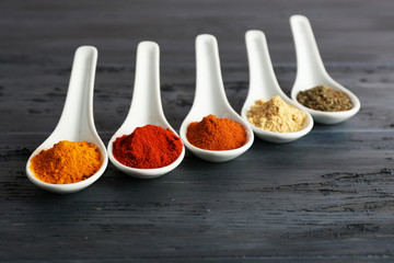Different kinds of spices in spoons on wooden background