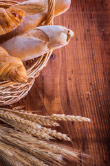 baguettes and croissants in wicker basket ears of wheat rye on v