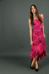 Beautiful young woman in long pink dress on dark gray background