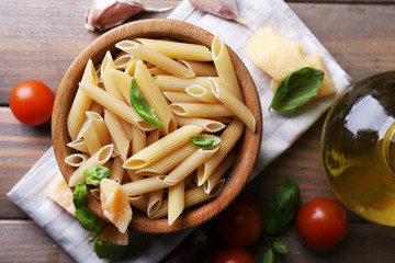 Raw pasta in bowl with cheese and vegetables on table close up