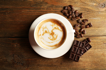 Cup of coffee latte art with grains and chocolate on wooden background