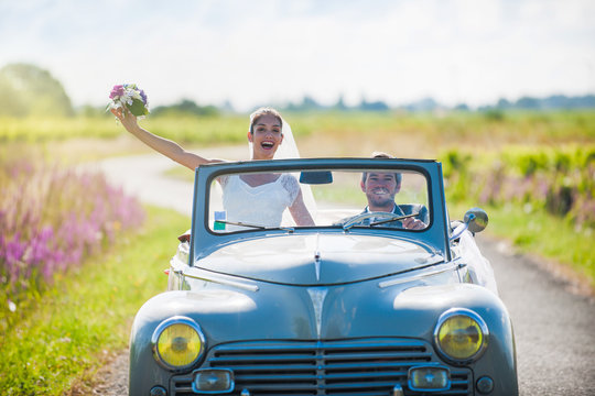 A newlywed couple is driving a retro car