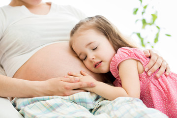 Obraz na płótnie Canvas Cute child girl embracing pregnant mother