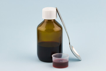 Glass bottle with spoon and dosage cup filled up red syrup