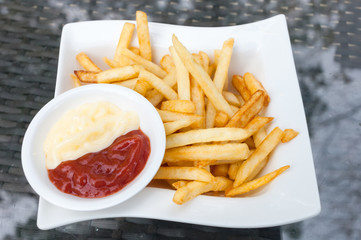 Tasty french fries in  white plates on glass table background