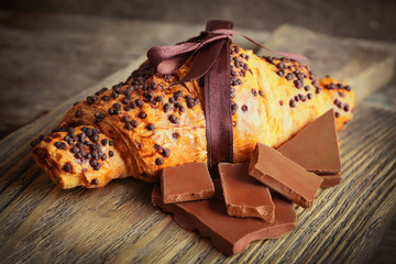 Fresh and tasty croissant with chocolate on wooden background