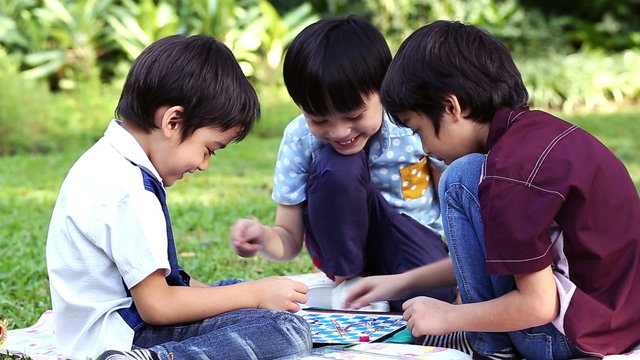 Three little boys playing a board game sitting in park