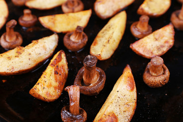 Baked potatoes with mushrooms and spices on pan close up