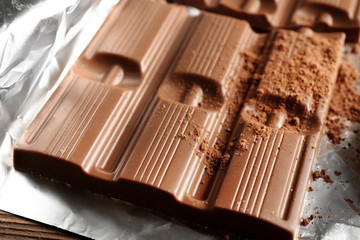 Bar of chocolate with cocoa on foil, closeup