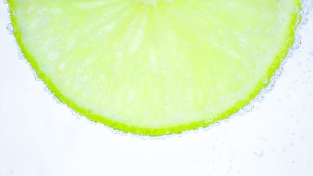Sparkling water with bubbles and lime slice on white