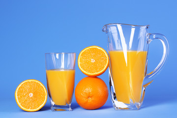 Glass and pitcher of orange juice on blue background