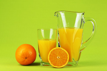 Glass and pitcher of orange juice on green background