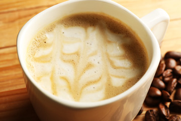 Cup of coffee latte art with grains on wooden table, closeup