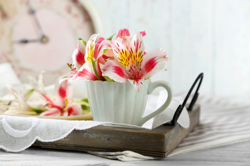 Beautiful flowers in cup, on wooden background