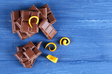 Pieces of chocolate with orange peels on color wooden