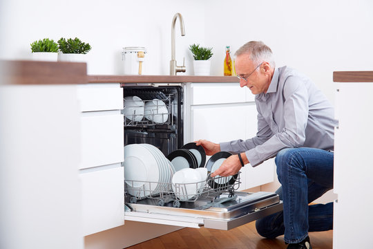 Senior man in kitchen, empty out the dishwasher 9