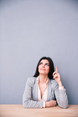 Thoughtful young woman sitting at the table and pointing up