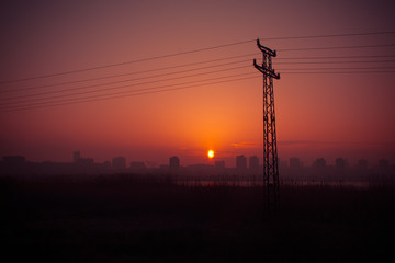 Fototapeta premium Power pole silhouettes in orange purple cloudy sunset background