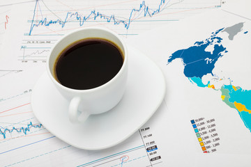 Coffee cup over world map and financial market charts