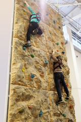 Two boys climbing up on practice wall in gym, rear view