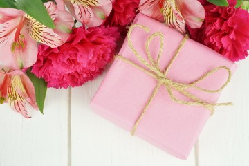 Gift box with pink carnation and lily flowers on white wood
