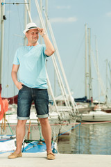 Fashion portrait of handsome man on pier against yachts