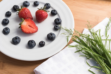 Plate with berries, bouquet of grass on white towel
