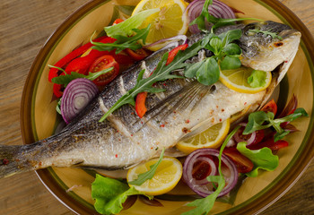Fried dorado fish on plate with fresh salad and lemon.