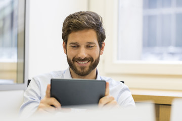 Cheerful man holding tablet pc in office