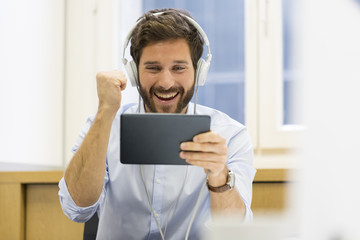 Happy man in office withe tablet pc and headphones