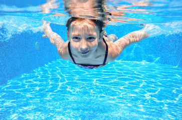 Happy girl swims in pool underwater, active kid swimming