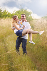 A cherry couple in the field. He is carying her in his arms.