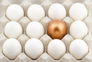 Golden egg arranged in the middle of white eggs in the carton 