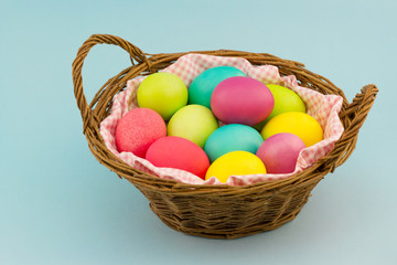  Wicker basket full of colorful painted eggs on blue background