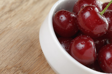 ripe cherry berries in white bowl on wood table