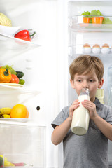 Cute boy drinking milk near open fridge