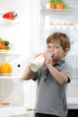 Funny little boy drinking milk near open fridge