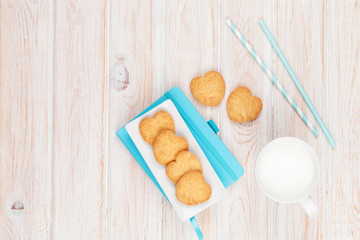 Cup of milk, heart shaped cookies and notepad