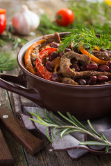 Beef with red bean and vegetables in pot on rustic background