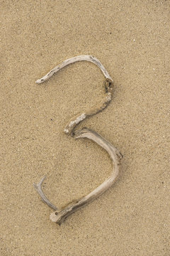 Zahl 3 aus Treibholz auf Sand