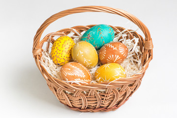 Hand-paited easter eggs in brown basket on white