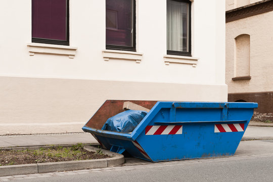 Ein blauer Container für Abfall steht vor einem Wohnhaus