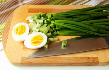 Egg, cut in half, and green onion on the board.