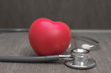 Red heart and stethoscope on wooden background.